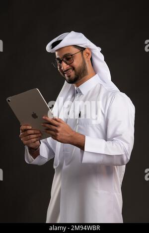 Arabischer Katar-Mann, der Tisch benutzt und auf isoliertem Hintergrund posiert. Männliches Modell in arabisch-katarischem Kleid auf isoliertem Hintergrund. Verschiedene Posen Stockfoto