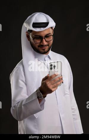 Arabischer Katar-Mann, der Tisch benutzt und auf isoliertem Hintergrund posiert. Männliches Modell in arabisch-katarischem Kleid auf isoliertem Hintergrund. Verschiedene Posen Stockfoto