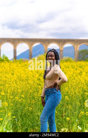 Lachte lächelnd, schwarzes ethnisches Mädchen mit Zöpfen, Reisende, auf einem Feld gelber Blumen Stockfoto