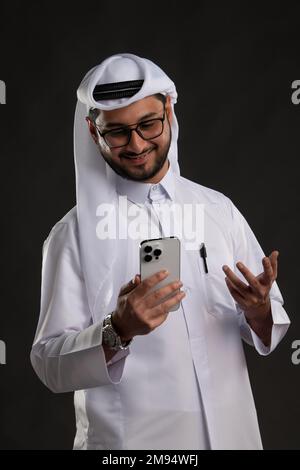 Arabischer Katar-Mann, der Tisch benutzt und auf isoliertem Hintergrund posiert. Männliches Modell in arabisch-katarischem Kleid auf isoliertem Hintergrund. Verschiedene Posen Stockfoto