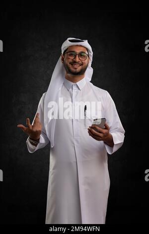 Arabischer Katar-Mann, der Tisch benutzt und auf isoliertem Hintergrund posiert. Männliches Modell in arabisch-katarischem Kleid auf isoliertem Hintergrund. Verschiedene Posen Stockfoto