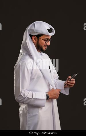 Arabischer Katar-Mann, der Tisch benutzt und auf isoliertem Hintergrund posiert. Männliches Modell in arabisch-katarischem Kleid auf isoliertem Hintergrund. Verschiedene Posen Stockfoto