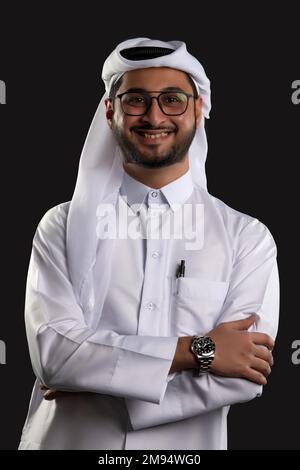 Arabischer Katar-Mann, der Tisch benutzt und auf isoliertem Hintergrund posiert. Männliches Modell in arabisch-katarischem Kleid auf isoliertem Hintergrund. Verschiedene Posen Stockfoto