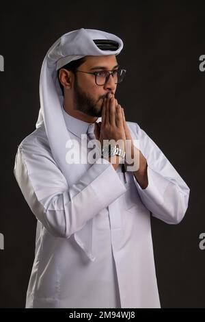 Arabischer Katar-Mann, der Tisch benutzt und auf isoliertem Hintergrund posiert. Männliches Modell in arabisch-katarischem Kleid auf isoliertem Hintergrund. Verschiedene Posen Stockfoto