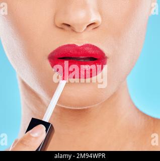 Ein Farbakzent. Studiofoto einer unbekannten jungen Frau, die Lippenstift vor blauem Hintergrund aufträgt. Stockfoto