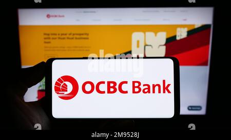 Person, die ein Mobiltelefon mit dem Logo der Oversea-Chinese Banking Corporation (OCBC Bank) auf dem Bildschirm vor der Webseite hält. Konzentrieren Sie sich auf das Display des Telefons. Stockfoto