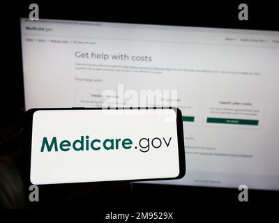 Person mit Smartphone mit Logo des US-Krankenversicherungsprogramms Medicare auf dem Bildschirm vor der Website. Konzentrieren Sie sich auf das Display des Telefons. Stockfoto