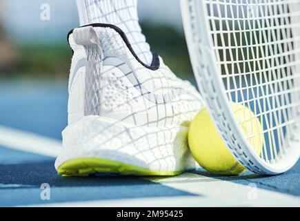 Das ist die einzige Möglichkeit, einen Tennisball zu sammeln. Ein nicht wiedererkennbarer Mann, der seinen Fuß und Schläger benutzt, um während des Trainings einen Tennisball aufzufangen. Stockfoto