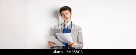 Geschäftsmann in Anzug durch Papiere suchen, Dokumente bei der Arbeit lesen und denken, Blick neben Logo, beschäftigt auf weißem Hintergrund stehen Stockfoto