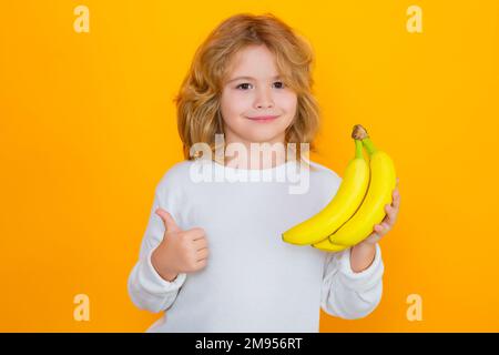 Kinderspiel-Banane im Studio. Studioporträt eines süßen Jungen mit Bananen isoliert auf Gelb. Stockfoto