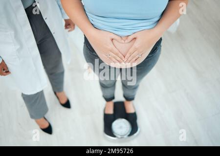 Eine nicht wiedererkennbare schwangere Frau, die sich in einer Klinik wiegt. Stockfoto