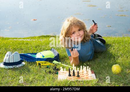 Der Junge zeigt Schachfiguren auf einem Schachbrett. Frühe Entwicklung. Ein Junge denkt über Schach im Sommerpark nach. Das Konzept des Lernens und des heranwachsenden Kindes Stockfoto