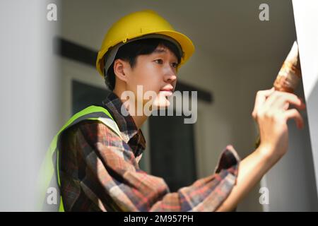 Professioneller Maler im Schutzhelm hält Pinsel in der Hand und streicht die Wand Stockfoto