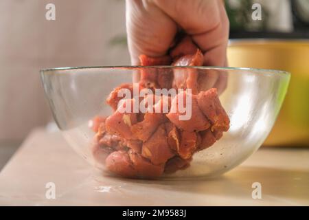 Ein Mann mischt Schweinefleisch, Rindfleisch, Hühnchen, truthahn mit Gewürzen, Salz, Pfeffer, Kräuter, Paprika in einer Glasschüssel. Marinieren von Fleisch in Gewürzen. Mittagessen kochen Stockfoto