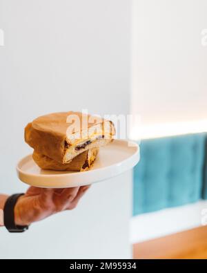 Ein unbekannter Mann hält im Restaurant ein frisch gebratenes Sandwich auf einem weißen Teller. Frühstückskonzept Stockfoto
