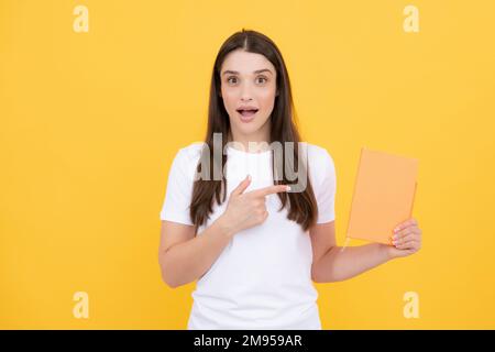 Lustiges, überraschtes Teenager-Mädchen mit Notizbüchern, die auf gelbem Hintergrund stehen, mit Kopierraum. Bildungskonzept für die Schule. Porträt eines jungen Schülers. Stockfoto