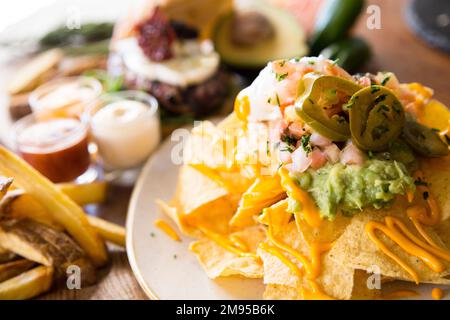 Nachos mit Guacamole. Nachos sind ein Gericht mexikanischer Herkunft, das aus Bratstücken von Maistortilla besteht, die mit einem speziellen Käse bedeckt sind. Stockfoto