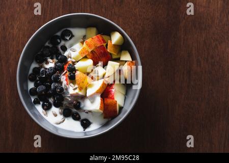 Gesunde Frühstückschüssel mit Obst und Joghurt auf einer hölzernen Oberfläche mit Scheiben von Apfel, schwarzen Johannisbeeren und Sonnenblumenkernen. Draufsicht, Kopierbereich. Stockfoto
