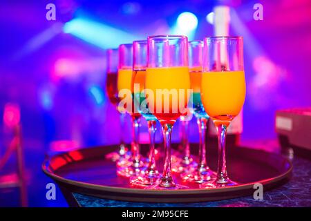 Gläser mit verschiedenen alkoholischen Getränken und Cocktails mit farbigem, verschwommenem Hintergrund auf der Feier im Nachtclub Stockfoto