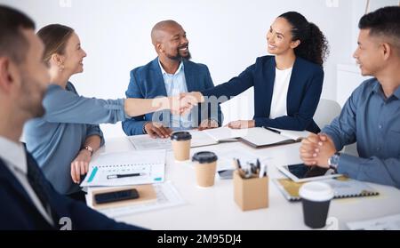 Ein Team aus lächelnden Geschäftsleuten, die sich im Büro nach einem Meeting im Sitzungssaal die Hände schütteln. Gruppe von glücklichen Profis und Kollegen mit Stockfoto