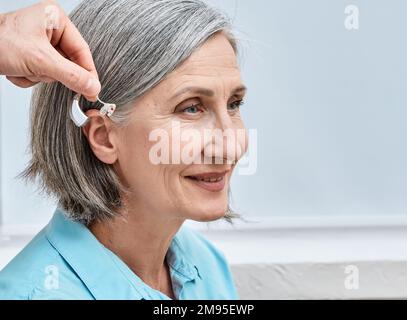 Installation eines Hörgeräts am Ohr einer Seniorin im Audiologiezentrum, Nahaufnahme, Seitenansicht. Schwerhörigkeitsbehandlung, Hörlösungen Stockfoto