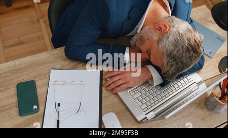 Langweiliger, schläfriger, alter Programmierer, Programmierer, Softwareentwickler im formellen Anzug, der nach Routinearbeiten an einem Laptop am Büroschreibtisch einschläft. Erschöpfter, müder Freiberufler, arbeitsahoischer Mann. Überarbeitet Stockfoto