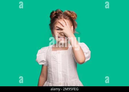 Lächelndes, glückliches Mädchen, das Hand auf Gesicht legt, Gesichtsschmerz isoliert auf einem grünen, hellen Studioporträt im Hintergrund. Stockfoto