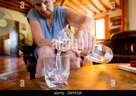 Senioren und Hitzewelle: Immer hydriert. Intensive Hitze: Alte Frau trinkt Wasser. Illustration, ältere Menschen und Hydratation, Dehydratationsrisiko Stockfoto