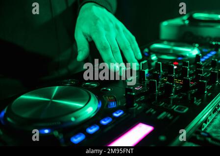 Handbewegung der DJ-Controller auf dem Music Control Panel im Nachtclub mit grüner Hintergrundbeleuchtung Stockfoto