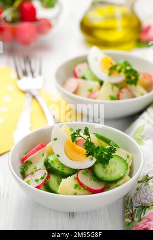 Gesunder Frühlingssalat mit Kartoffeln, gekochten Eiern, Radieschen und Gurken mit grünem frischem Dill in einer weißen Schüssel. Stockfoto