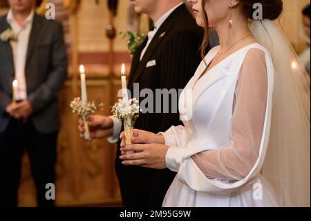 Die Hochzeit in der Kirche, das Sakrament der Hochzeit in der Kirche, die Hände der Braut und des Bräutigams im Detail und aus der Nähe. Stockfoto