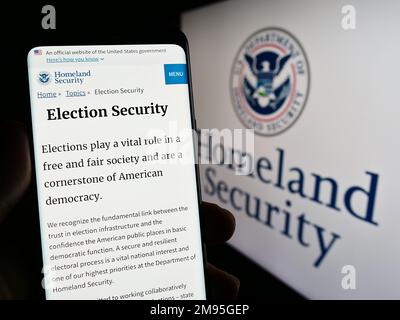 Person, die ein Smartphone mit einer Webseite des US Department of Homeland Security (DHS) auf dem Bildschirm vor dem Siegel hält. Konzentrieren Sie sich auf die Mitte des Telefondisplays. Stockfoto