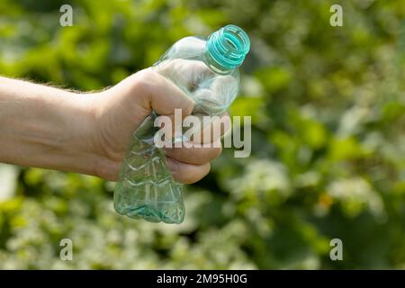 Hand hält zerbrochene leere Plastikflasche im Park Stockfoto