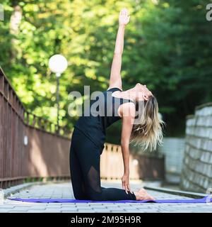 Frau führt einen gesunden Lebensstil und praktiziert Yoga, führt eine Variation der Ushtrasana-Übung mit einem Arm angehoben, Kamel Pose, trainiert alon Stockfoto