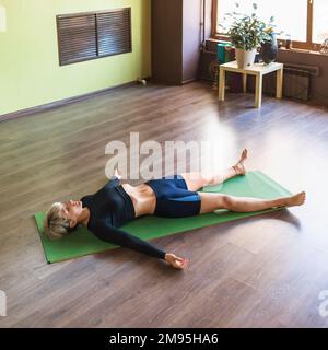 Frau, die Yoga macht, Shavasana-Übung mit Pranayama-Atmung macht, Asana entspannt, auf einer Matte im Zimmer liegt Stockfoto