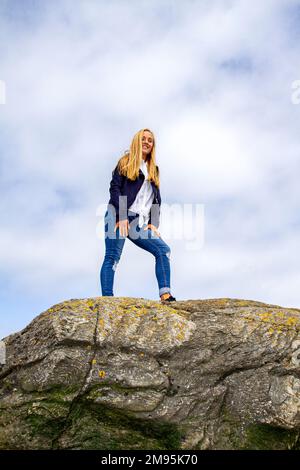 Rhianna Martin, eine wunderschöne blonde Frau, steht hoch auf den Felsen und genießt das warme Wetter am Wormit Beach in Fife County, Schottland, Großbritannien Stockfoto