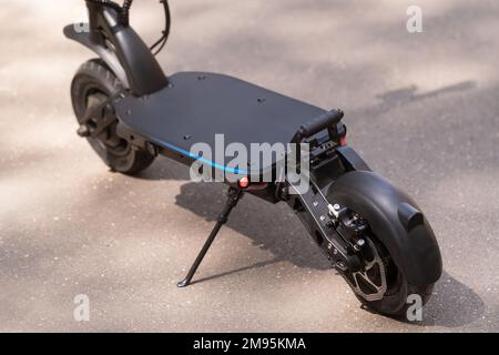 Schwarzer elektrischer Roller, der auf dem Trittbrett auf der Straße steht. Stockfoto