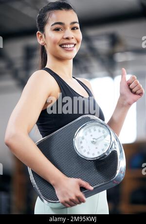 Ich bin auf dem besten Weg, mein Zielgewicht zu erreichen. Porträt einer fit-jungen Frau, die eine Waage hält und Daumen nach oben zeigt. Stockfoto