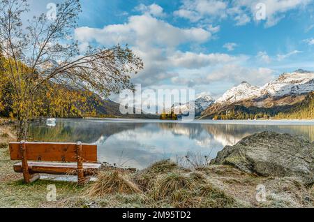 Einsame und leere Bank in Herbstlandschaft am Lake Sils, Engadine, Schweiz, mit Piz Margna im Hintergrund Stockfoto