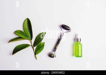 Zutaten für natürliche Schönheitsbehandlungen. Öl aus Kräutern, Gesichtswalze und grüner Pflanze. Draufsicht, flaches Legen, Kopierbereich, Modell. Stockfoto