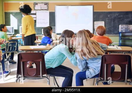 Studenten, Freunde und flüstern im Klassenzimmer nach Geheimnissen, Klatsch oder Plaudern während des Unterrichts. Hinterhältige weibliche Lernende, die ruhige Informationen teilen Stockfoto