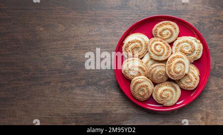 Zuckerspiralkekse auf dem roten Teller auf dem Holztisch, Banner mit Kopierbereich. Hausgemachte runde Kekse, Draufsicht. Gebäck-Konzept Stockfoto