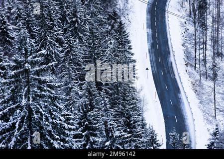 Freiburg, Deutschland. 17. Januar 2023. Schnee liegt neben einer Straße, während schneebedeckte Nadelbäume auf der linken Seite des Bildes zu sehen sind. In den letzten Tagen waren einige Zentimeter Schnee gefallen, und laut Meteorologen werden in den nächsten Tagen weitere Zentimeter Schnee erwartet. Kredit: Philipp von Ditfurth/dpa/Alamy Live News Stockfoto