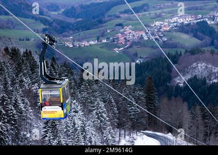 Freiburg, Deutschland. 17. Januar 2023. Ein Passagier fährt in einer Gondel der Schauinsland-Seilbahn über schneebedeckte Bäume in das Tal, während ein schneefreies Dorf im Hintergrund zu sehen ist. In den letzten Tagen waren mehrere Zentimeter Schnee gefallen, und Meteorologen zufolge werden in den nächsten Tagen weitere Zentimeter Schnee erwartet. Kredit: Philipp von Ditfurth/dpa/Alamy Live News Stockfoto