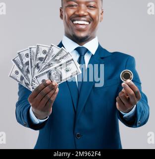 Würdest du es für die Belohnung riskieren? Studiofoto eines jungen Geschäftsmanns mit US-Dollar und einer Bitmünze vor grauem Hintergrund. Stockfoto