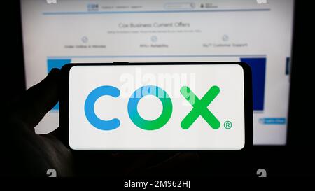 Person, die ein Smartphone mit dem Logo des US-Kabelfernsehunternehmens Cox Communications Inc. Auf dem Bildschirm vor der Website hält. Konzentrieren Sie sich auf das Display des Telefons. Stockfoto