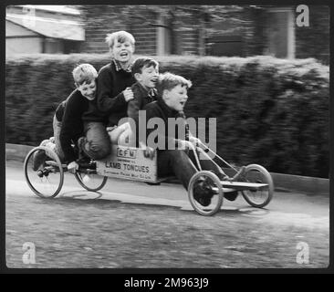 Vier Jungs auf einem selbstgemachten Go-Kart aus einer Kiste, die einst gefrorene Lammzungen enthielt, in Horley, Surrey. Zwei der Jungs gehören dem Fotografen und sie haben alle Spaß. Stockfoto