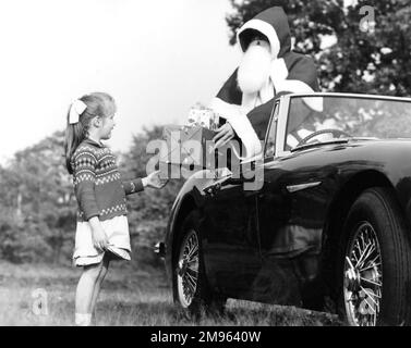 Ein kleines Mädchen bekommt ein Geschenk vom Weihnachtsmann, der jeden Tag einen Sportwagen einem Schlitten vorzieht Stockfoto