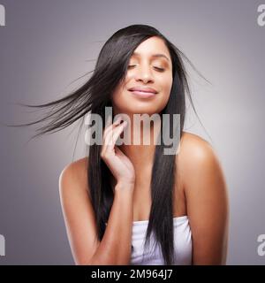 Ich habe mich noch nie so zuversichtlich gefühlt. Eine attraktive junge Frau, die allein im Studio steht und posiert, während ihr Haar im Wind weht. Stockfoto