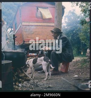 In einem Lager in Surrey sitzt ein alter Zigeuner auf einer Dose in der Nähe des Feuers Stockfoto